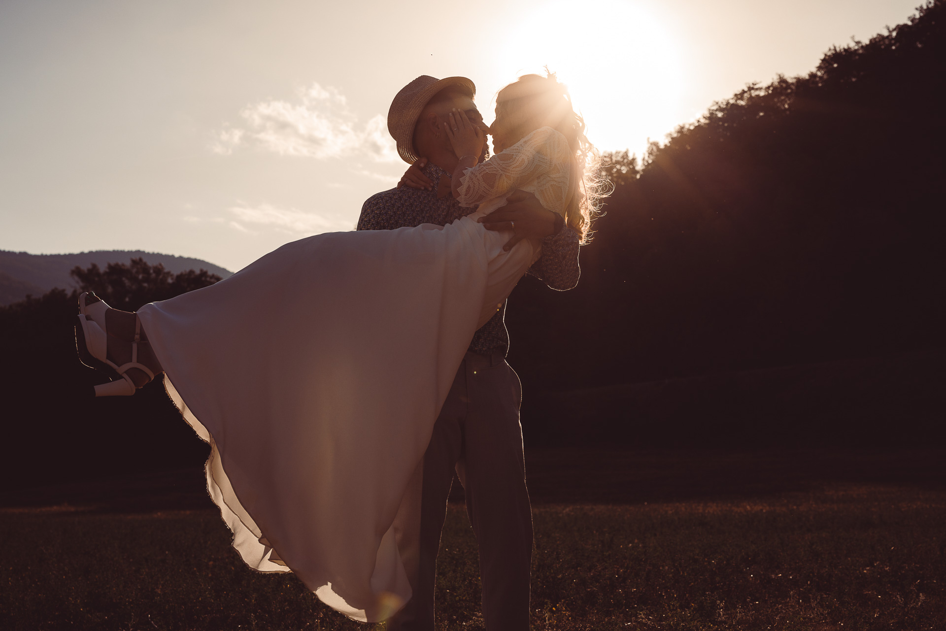 Groom lifting the bride at sunset in a mountain meadow